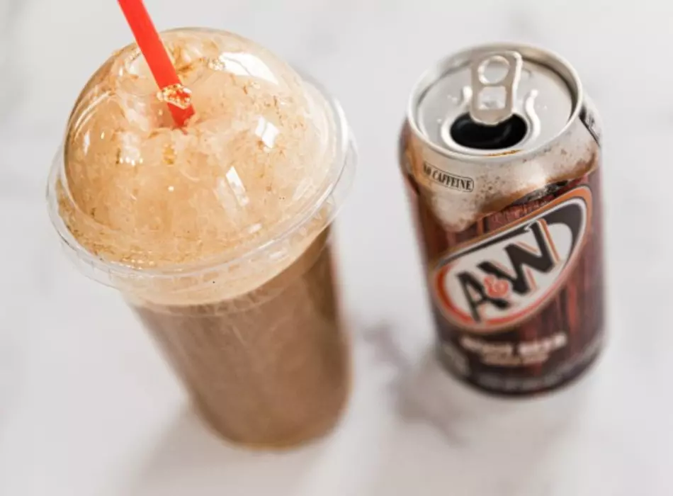 Root beer float with vanilla ice cream in a cup with lid and straw next to a can of A&W root beer