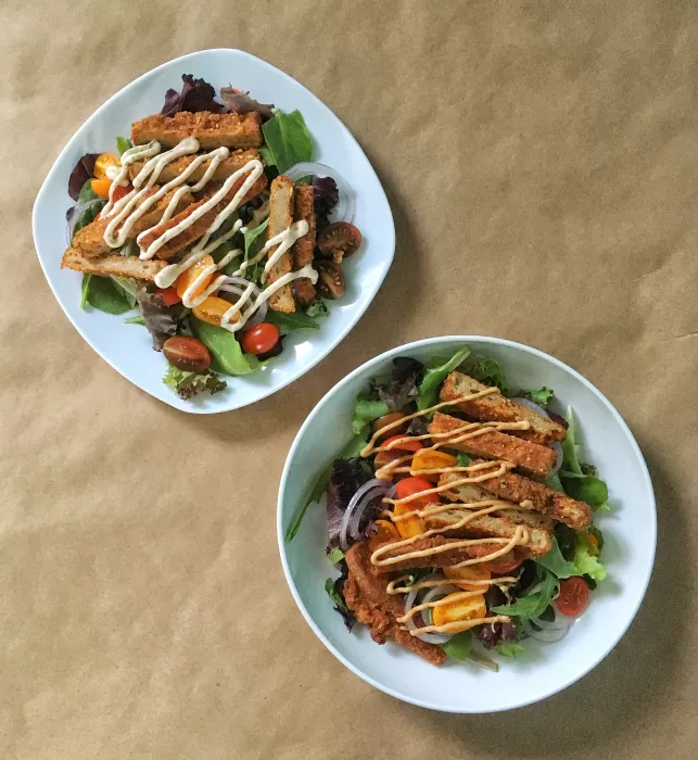Two salads, viewed from above, on white plates.