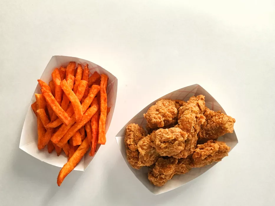 A fry boat of sweet potato fries next to a fry boat of crispy, craggy nuggets.